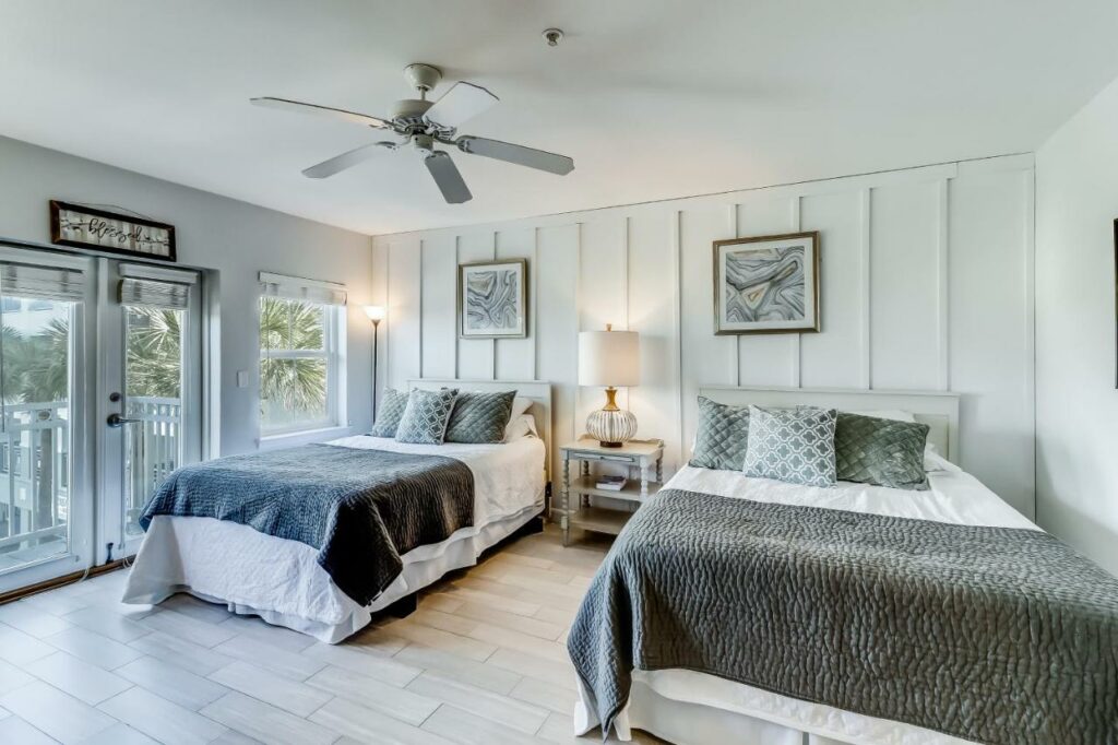 Two full beds in grey color schemes take up a room that features a balcony that overlooks the water at one of the places you must consider when looking for where to stay in Destin. 