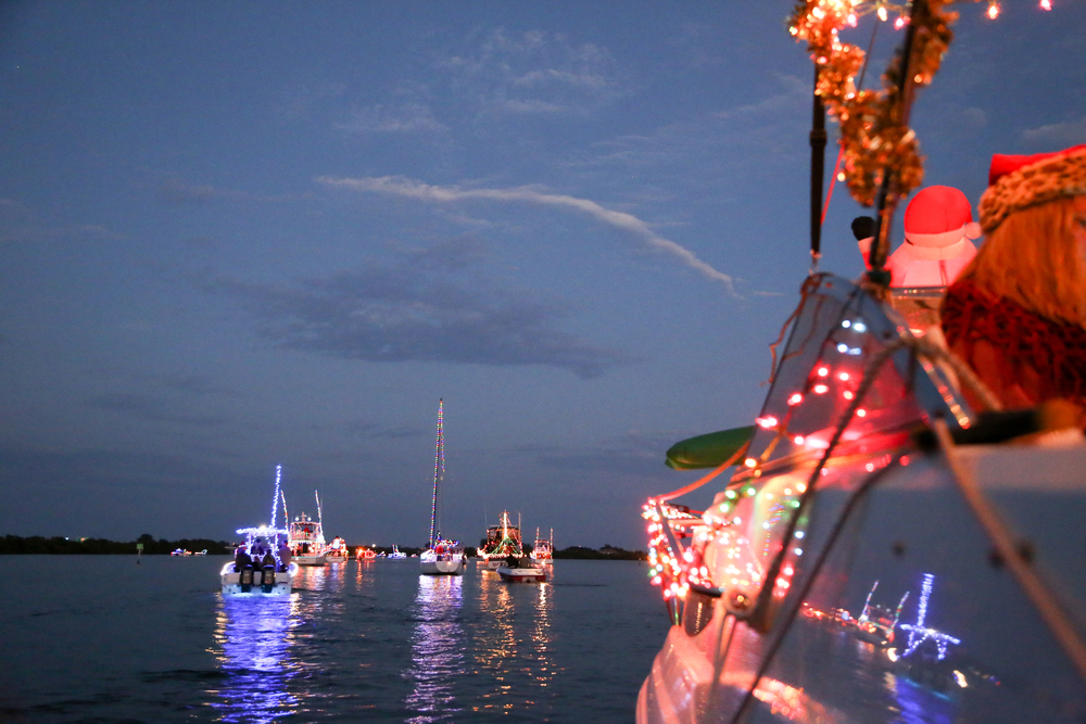 A parade of small boats proceeds through the water, each decorated with Christmas lights, similar to the boat parade in Tampa which is a fun way to see Christmas lights in Florida.