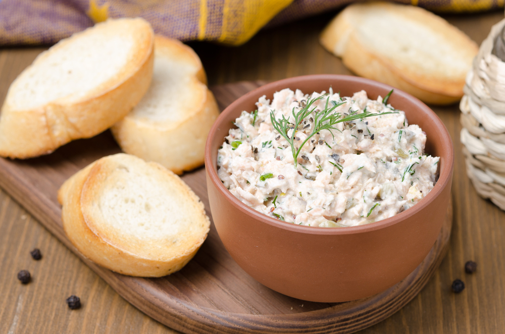 Small, round slices of baguette sit on a wooden tray next to a bowl of fish dip, which is a popular menu item at the best restaurants in Marathon.