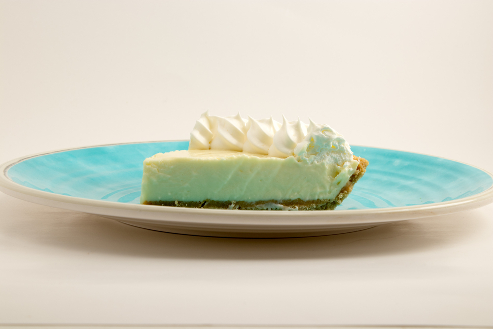 A slice of Key Lime Pie topped with coconut whipped cream sits on a teal ceramic plate, a popular menu item at the best restaurants in Marathon.