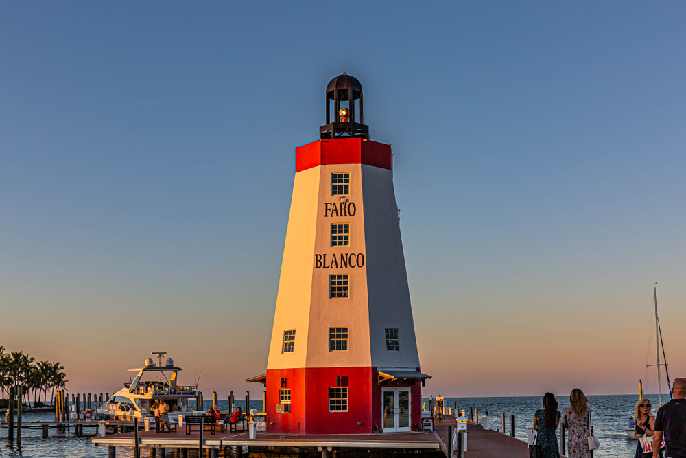 The Faro Blanco Lighthouse stands by the water at sunset, where people gather for dinner and drinks at one of the best restaurants in Marathon.