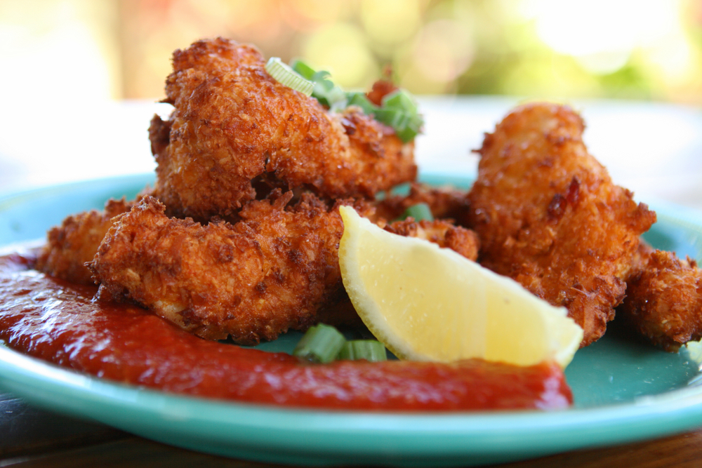 Fried conch fritters sit on a blue ceramic plate, with a wedge of lemon and cocktail sauce.