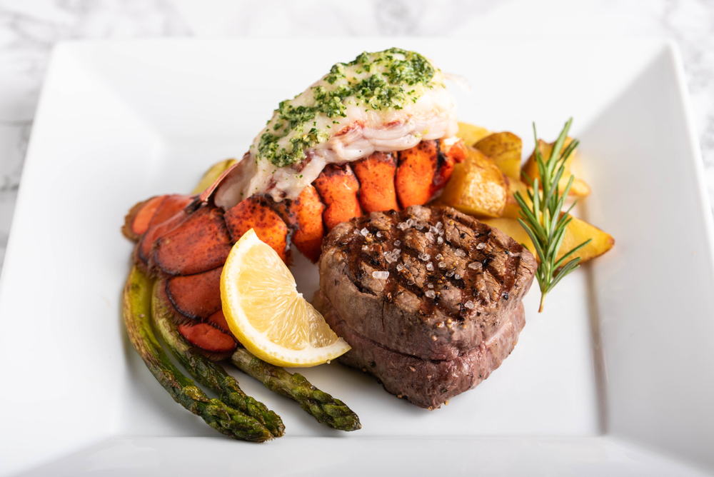 A "surf and turf" plate, with steak, a lobster tail, asparagus, potatoes, and a sprig of rosemary.