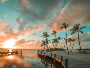 beautiful orange and teal sunset over calm waters and docks that stretch into the ocean decorated with palm trees!