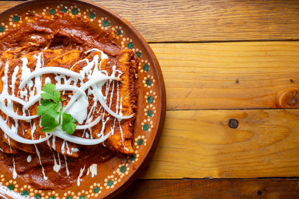 a beautifully decorated plate on a wood table, filled with awesome looking enchilada's ready to be devoured!