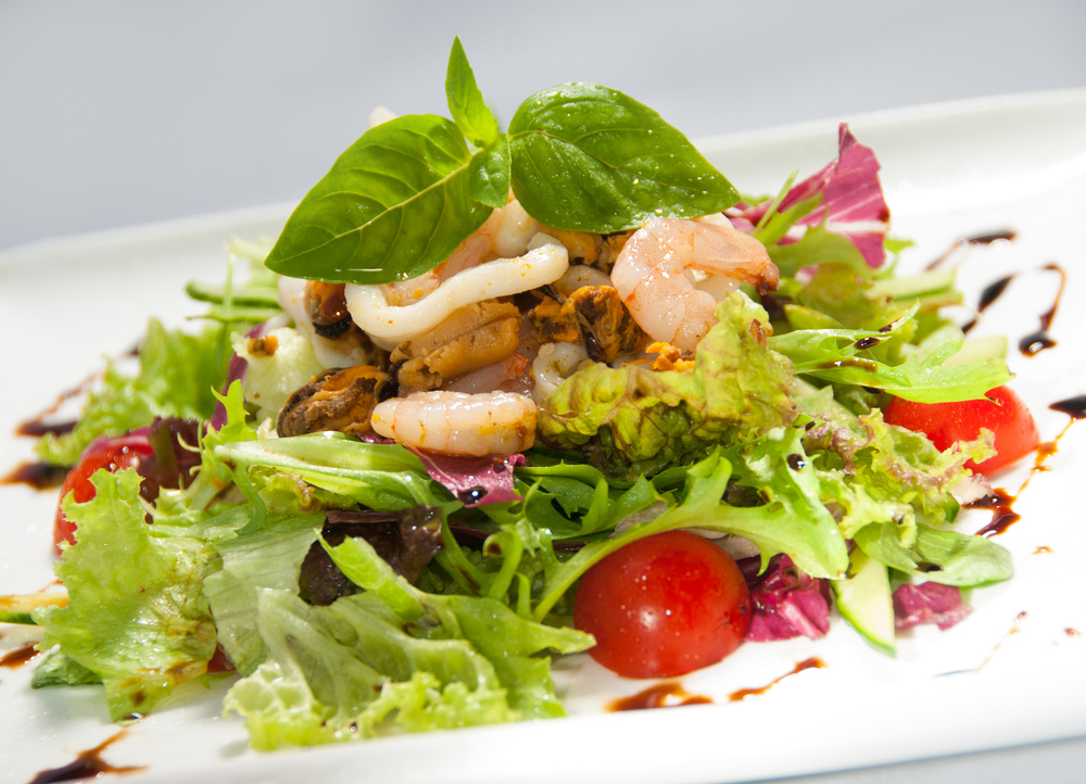 a seafood salad topped with shrimp and calamari over greens with tomatoes