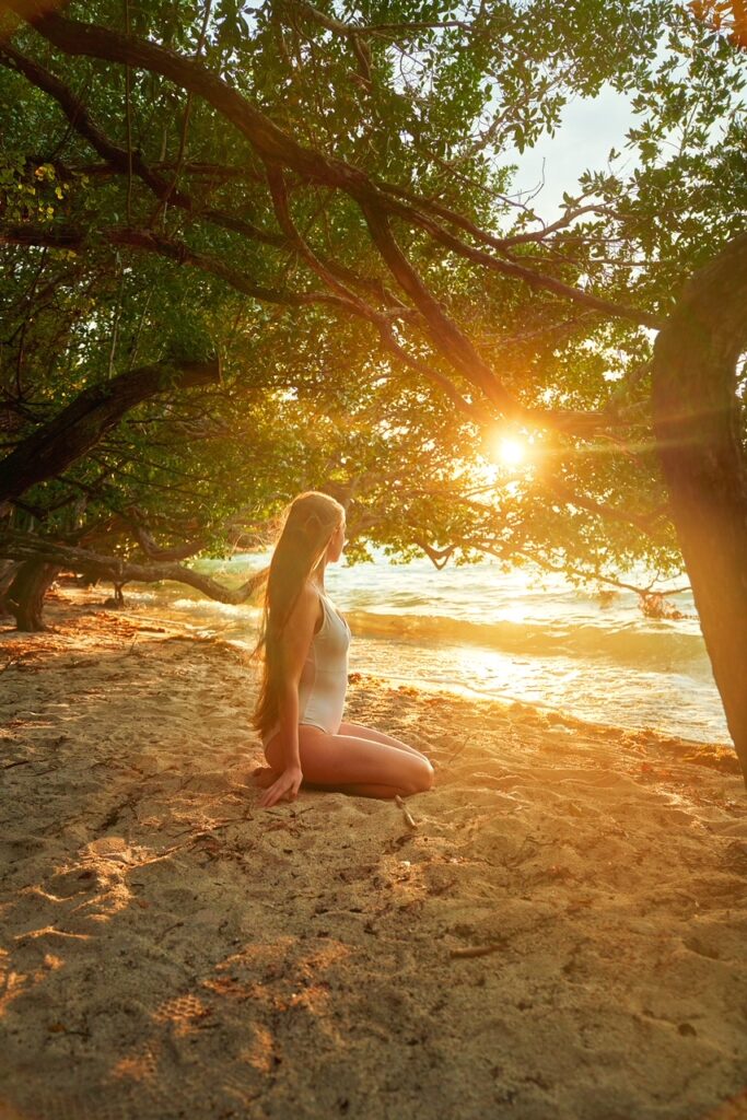 great sun setting through tree foliage as Victoria sits in the sand on a beach