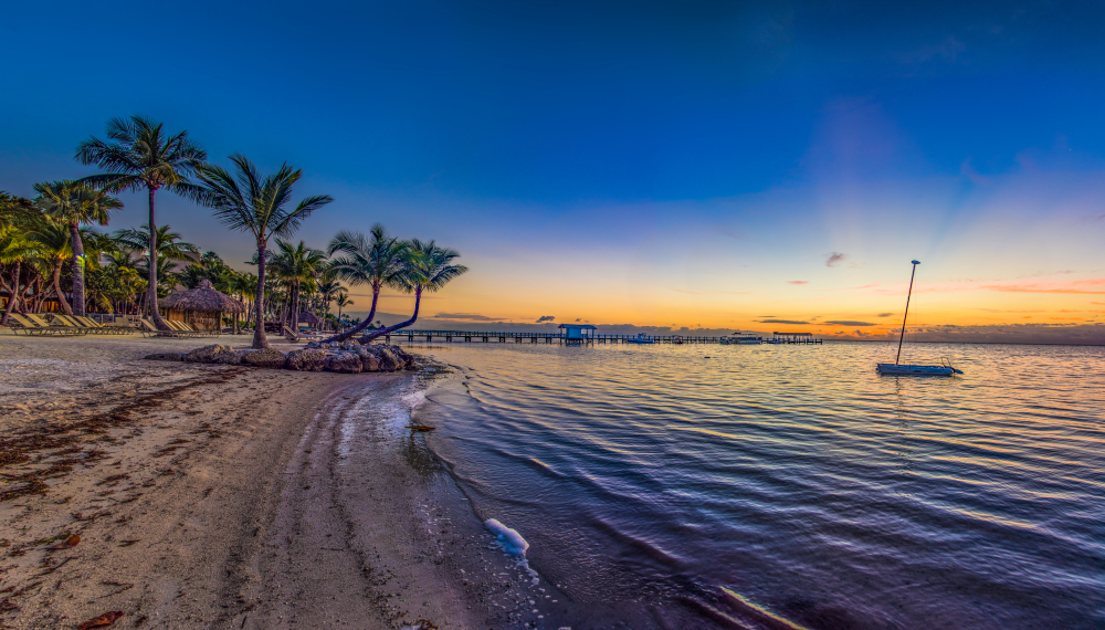 Islamorada Florida Keys Cheeca Lodge Resort Panorama at Sunrise. You can see an empty beach with a boat in the water and the sun setting. 