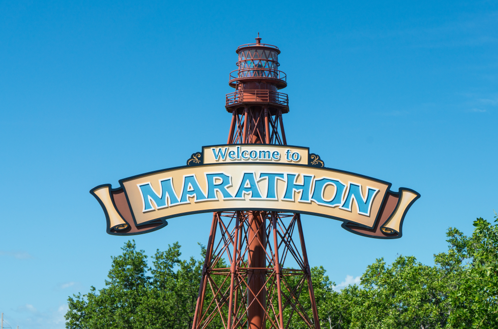 A picture of a dark orange lighthouse that has a sign that says welcome to marathon in bright blue letters