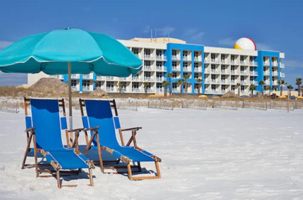 blue beach chairs with an umbrella on the white sand with a blue and white building at the back best beachfront hotels in destin