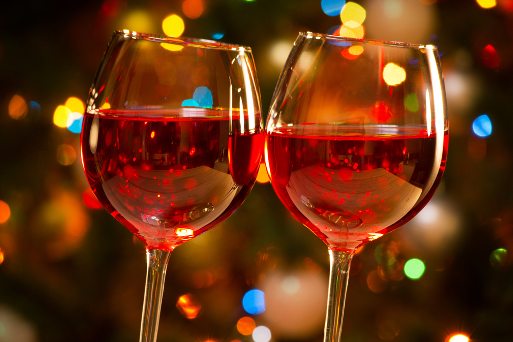 Red wine glasses in front of colorful Christmas lights.
