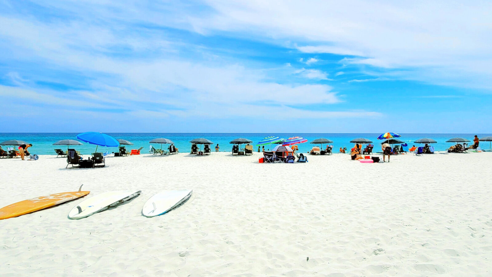 umberllas and surf boards laid out on a white sand beach on beat beaches on the Gulf Coast