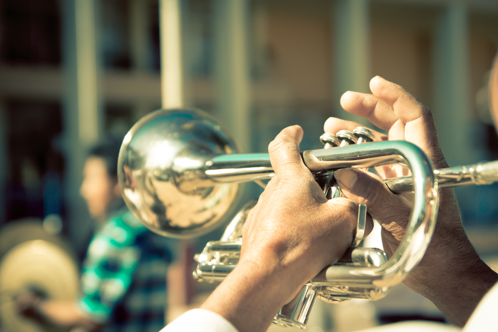 A closeup of hands playing a trumpet outdoors in the sun.