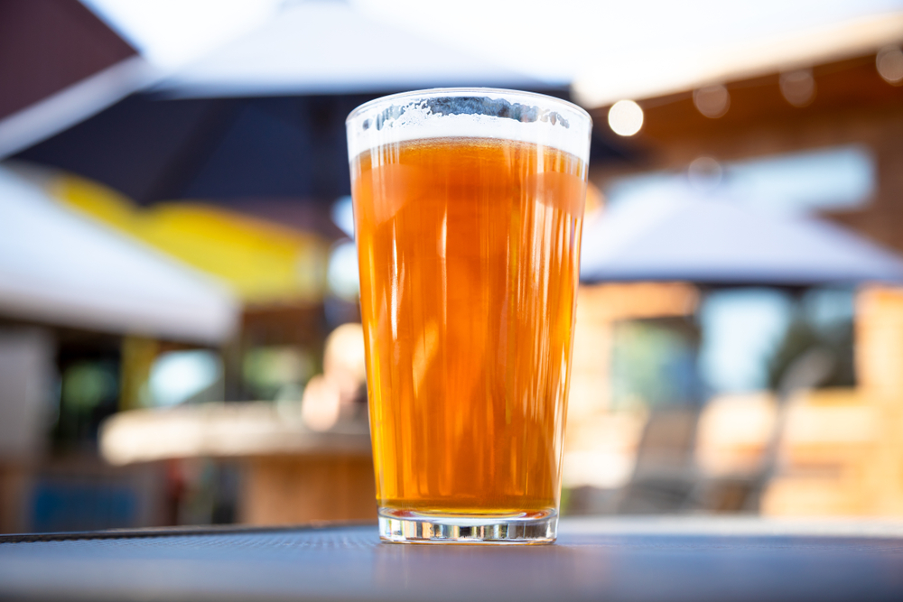 Tall glass of pale ale sitting on a table outside.