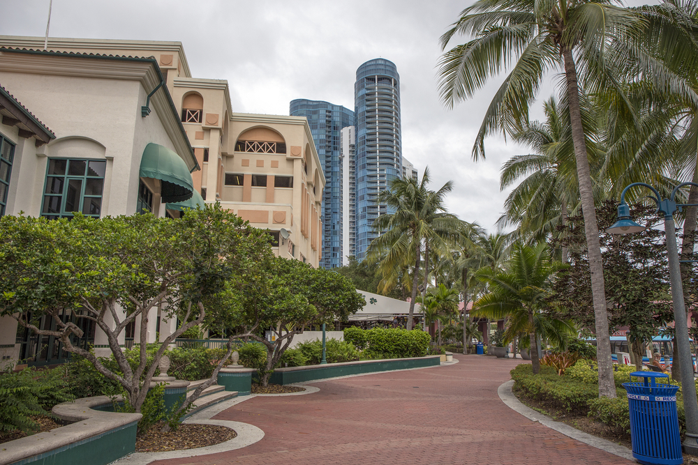 The brick riverwalk winds through trees and buildings in downtown Fort Lauderdale on an overcast day.