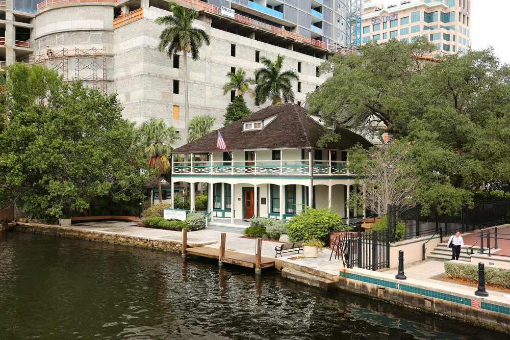 The two-story historic Stranahan House Museum sits along the riverwalk, with tall buildings in the background in Fort Lauderdale.