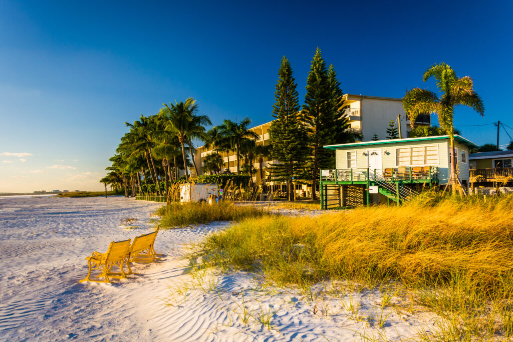 Fort Myers beach with a beach building and two chairs. There are trees and the water is in the background. 