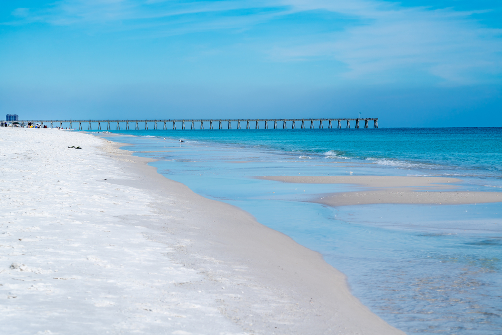 Pensacola beach showing the beach and the sea with people in the background by the pier