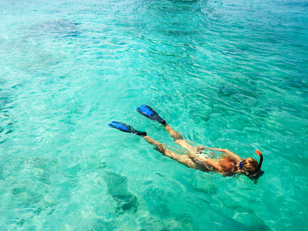 Young woman is snorkeling in blue water in an article about Florida in July 