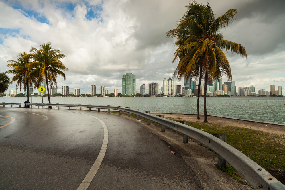 Beautiful Miami skyline along Biscayne Bay with rain clouds. There are buildings in the background and a road in the foreground