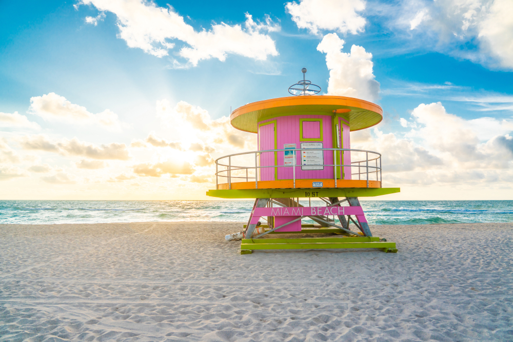 A bright pink and yellow lifeguard hut on Miami Beach with bright blue water on a sunny day in Florida in June