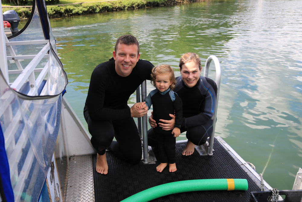 A family gathers at the end of a boat In wetsuits at crystal river. They have gone swimming with manatees, which is a unique option of something to do in Orlando with kids. 