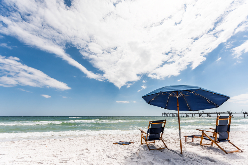 A set of beach chairs and an umbrella on a white sandy beach on a sunny day