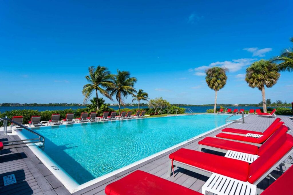 Big pool with red, lounge chairs next to the ocean.