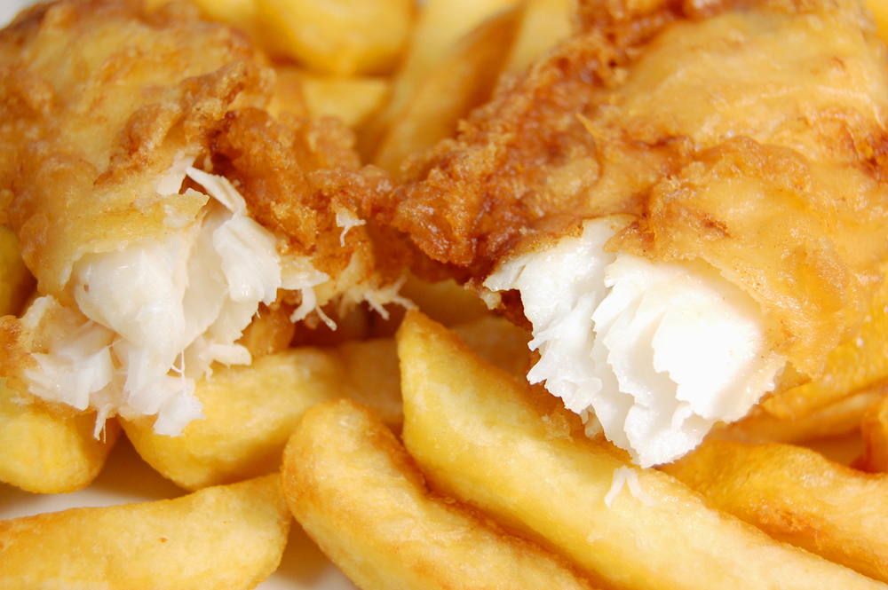 A close up of a piece of fried fish torn in half sitting on top of golden French fries.