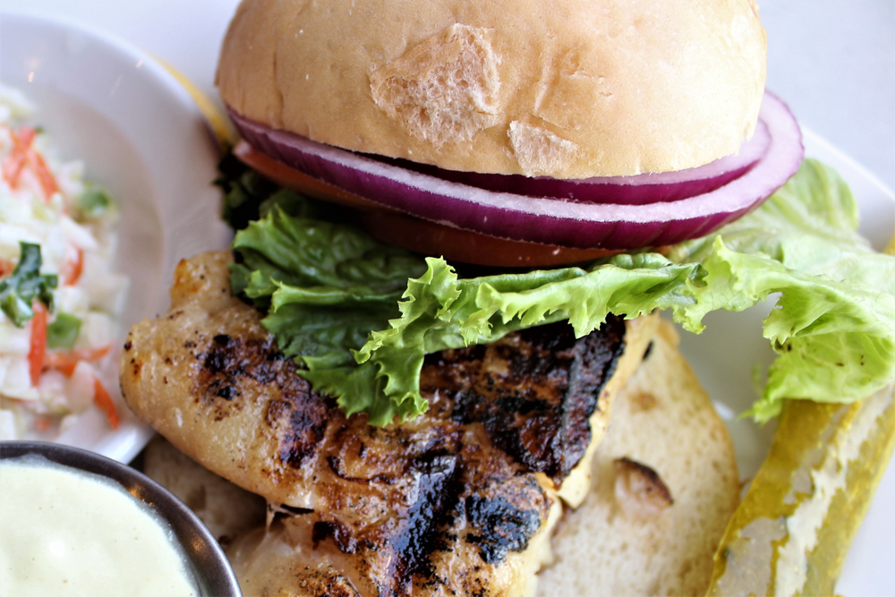 A blackened piece of grouper is wedged between a bun with lettuce and onion, like the grouper sandwich at Bayside Seafood, one of the best seafood restaurants in Naples.