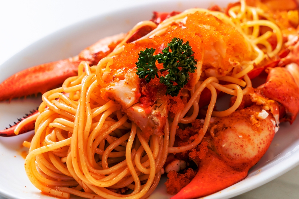 A close up of spaghetti and lobster meat set between lobster claws on a white plate.