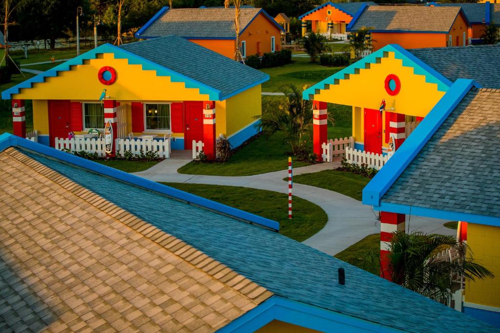 Beach style lego cabins around grass. They are red, blue and yellwo with small white fences.   