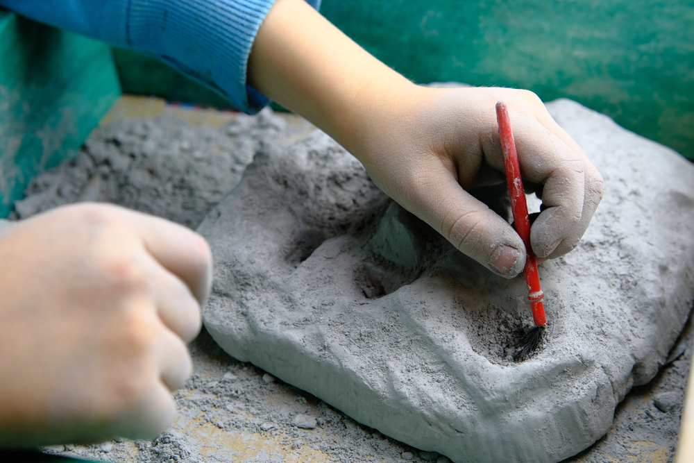 Child playing fossil, mineral and treasure excavation game. Child is using tools, such as a brush.