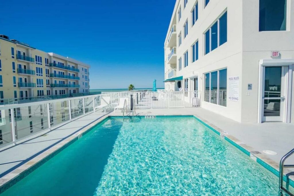 A rooftop pool where you can see the ocean on a bright white hotel