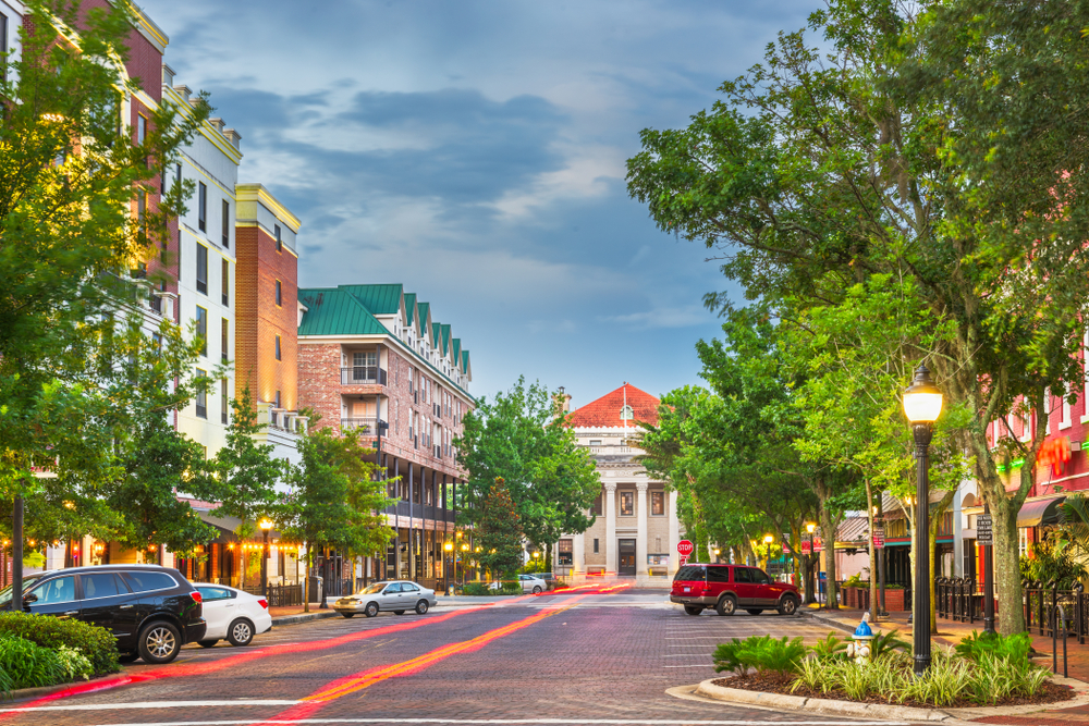 The buildings along downtown Gainesville at dusk, with four cars parked along the street and street lamps twinkling.