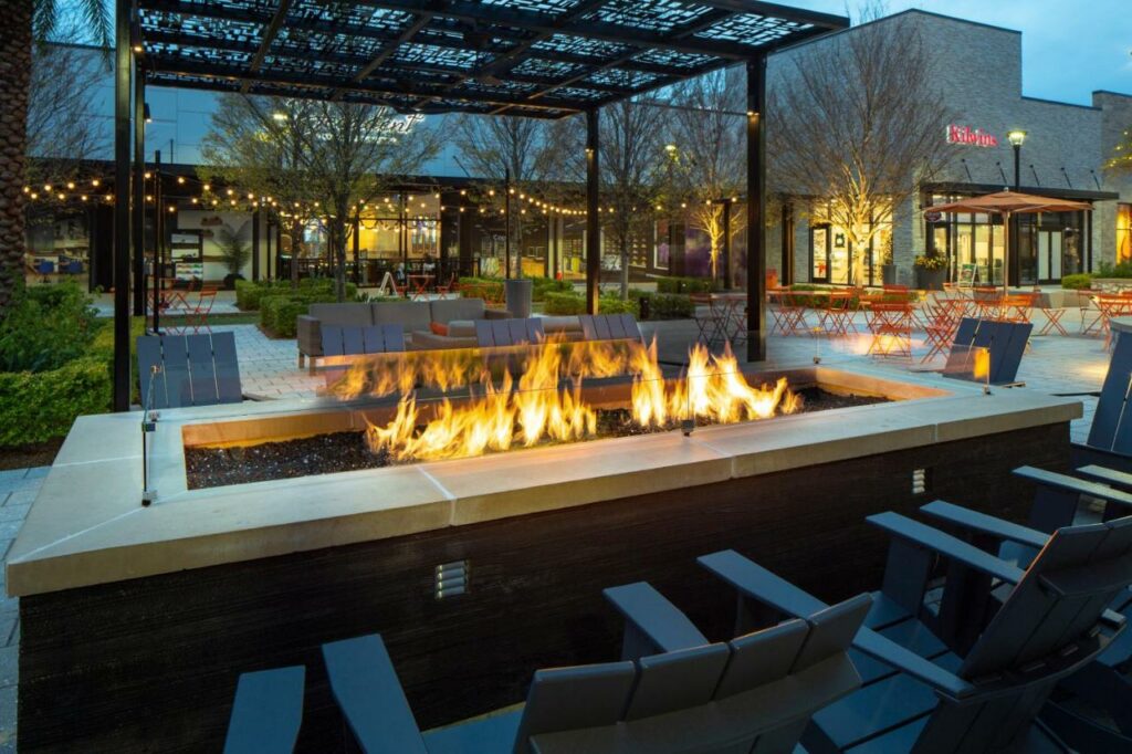 Outdoor seating area with a roaring firepit and string lights at dusk.