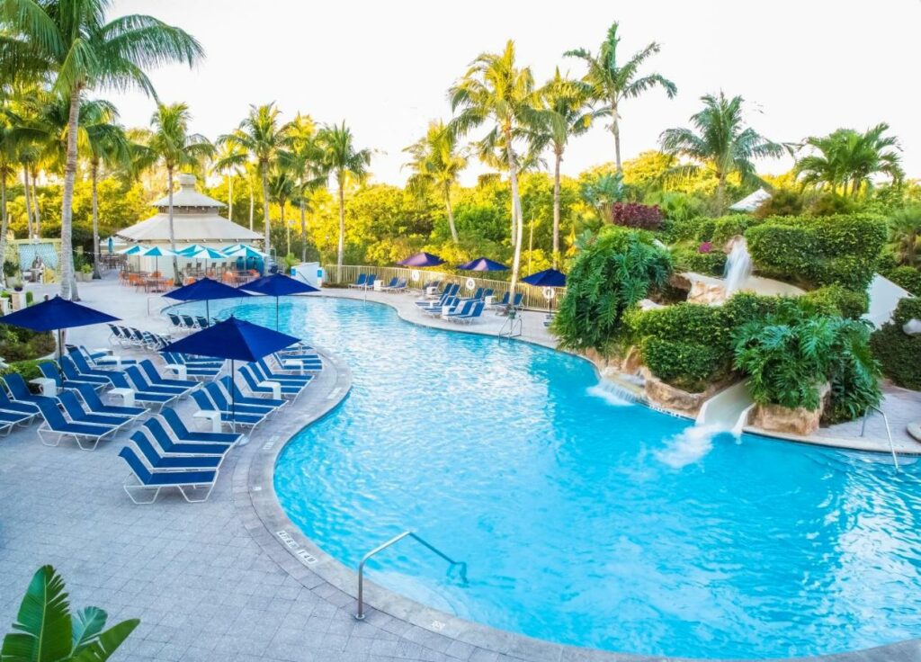 Pool area at Naples Grande Beach Resort with pool loungers, palm trees, and water slides.