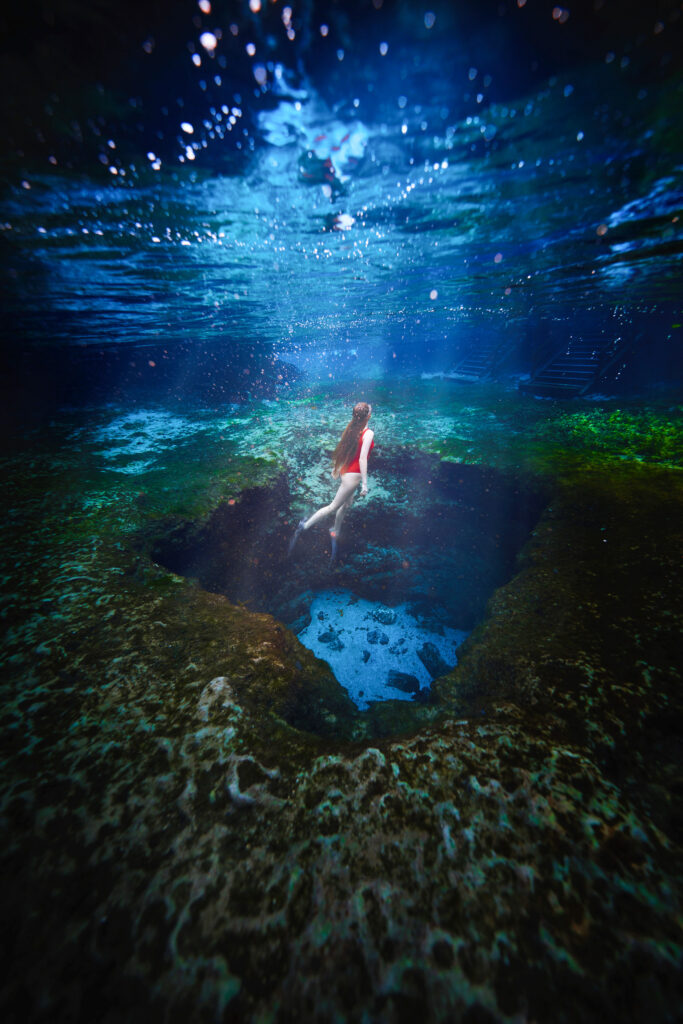 Underwater photo of a woman swimming above one of the caves in the clear spring water.