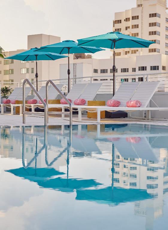 the art deco pool at the Grey with turquoise umbrellas and pink beach towels surrounded by the buildings of miami on this rooftop setting
