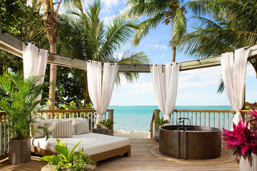 A view of a private balcony with soaking tub with the ocean int he background with palm trees at one of the best adults only resorts in Florida