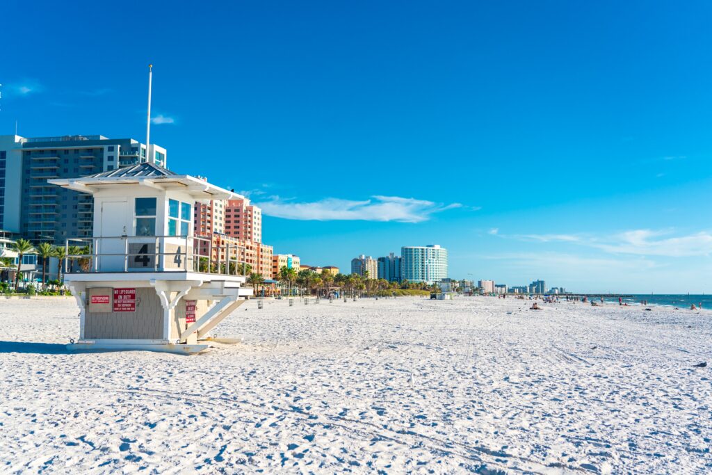Lifeguard tower on the beach with hotels in the background. The article is about the best beach resorts In Clearwater. 