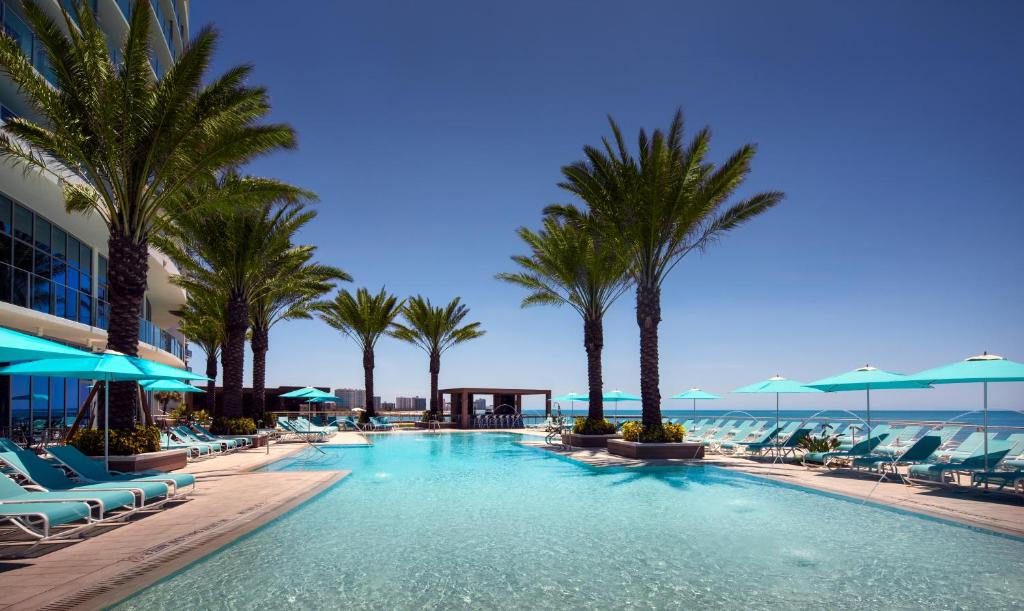 Huge hotel pool with a view of the ocean. the pool has loungers and palm trees around it.  