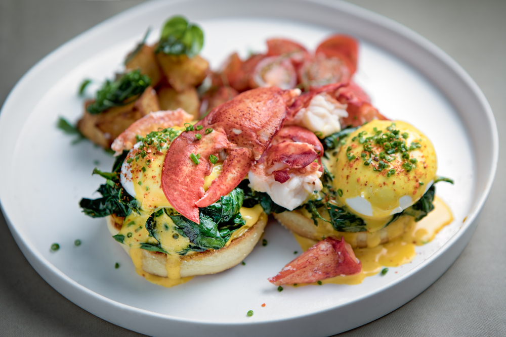 Eggs Benedict with lobster served on a round plate with sauteed potatoes. 