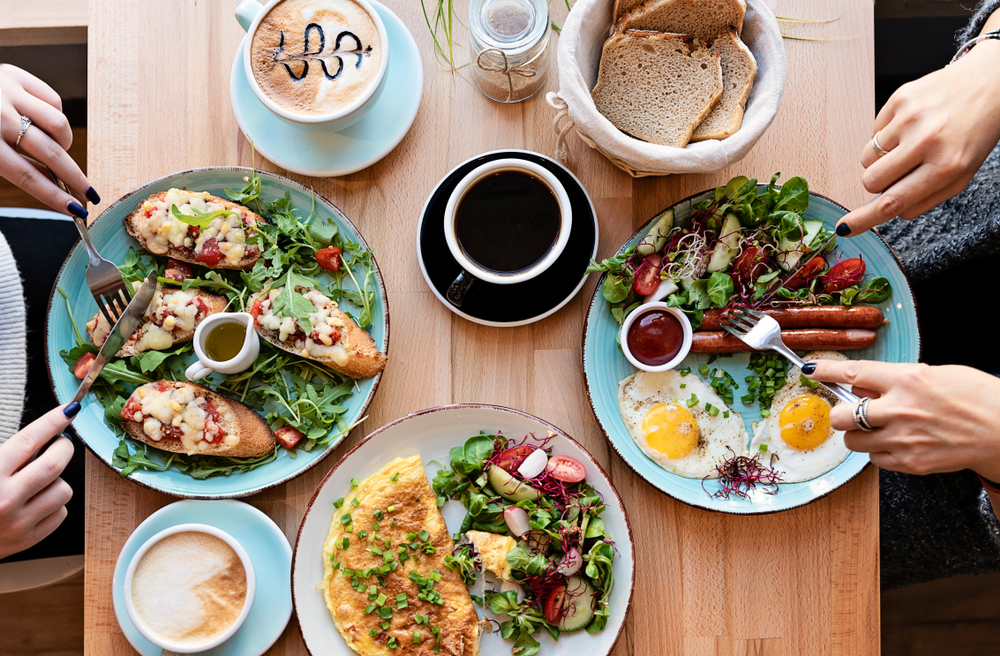 Two women enjoying brunch dishes like eggs and bacon, frittata, and baked savory dishes with coffee