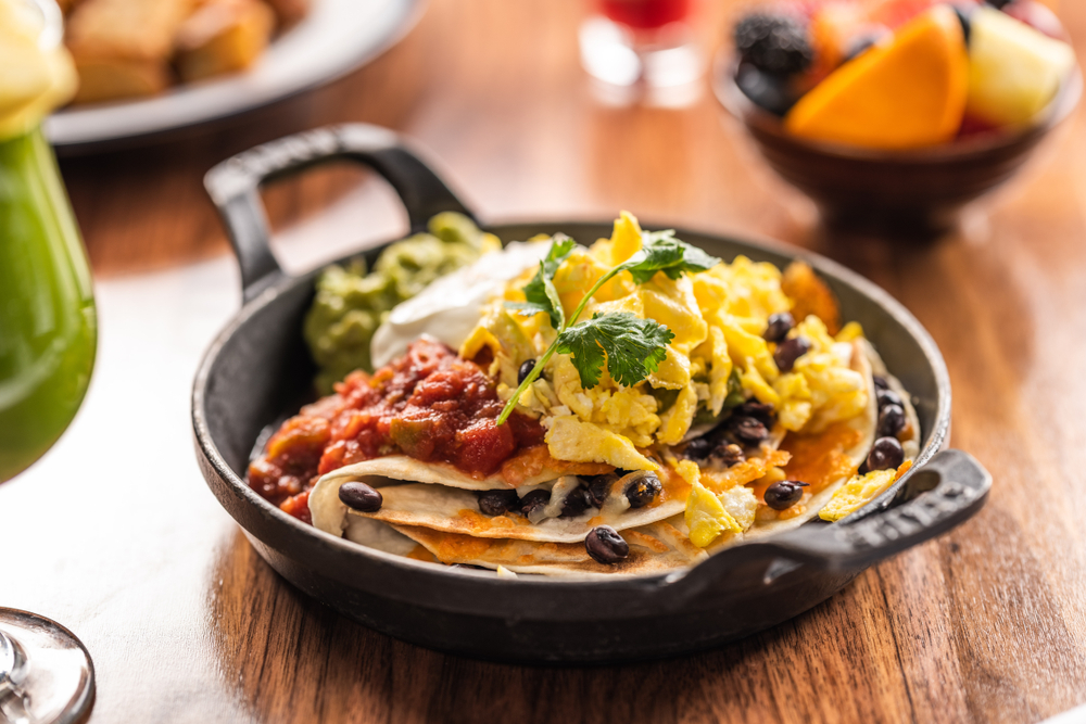 a skillet of huevos ranchros with tortilla, eggs, salsa, guac, beans and more