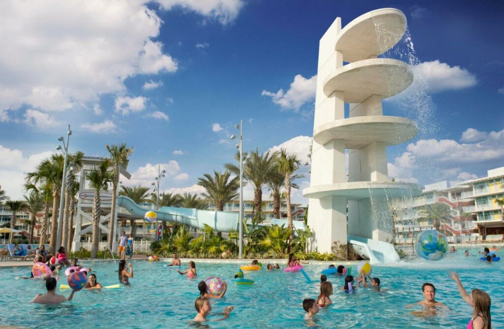 Kids play in a deep pool at Cabana Bay, which is one of the  best waterpark hotels in Orlando. A slide and diving tower can be seeing the background as they play in the water. 