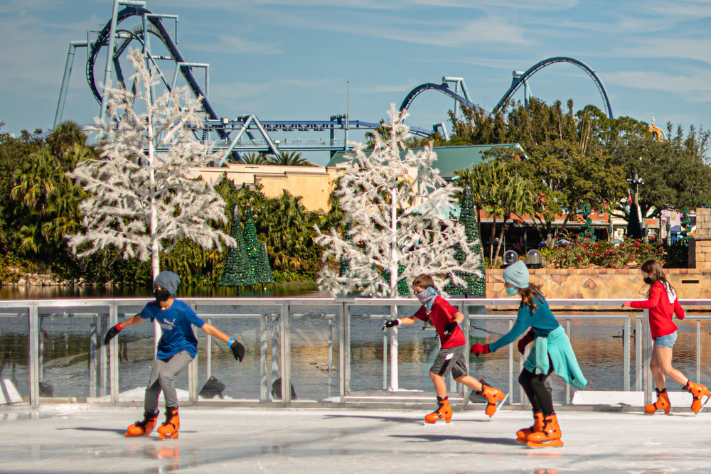 Kids go ice skating on fake ice in jackets and hats in Seaworld. The coaster loops behind them in the background, and this is only one of the many things you can do in Florida in December to celebrate the holidays. 