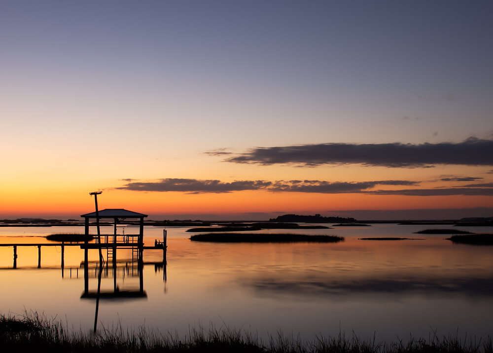 An orange sunset over the marshes of Cedar Key, FL with a fishing pier in silhouette.