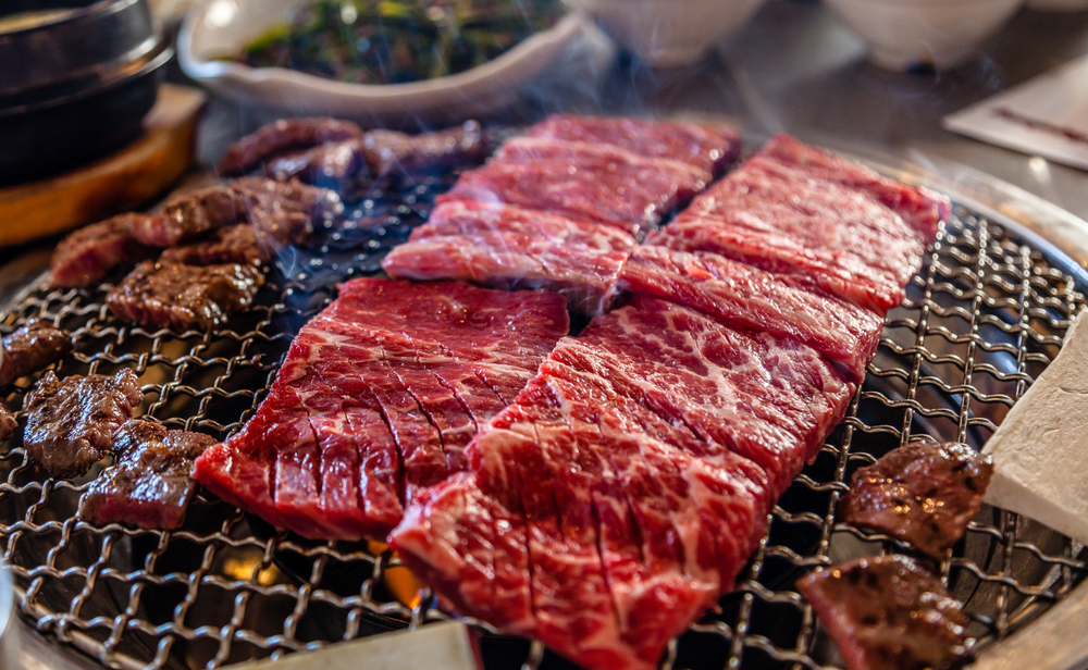 Slices of meat cook on a tabletop grill at a Korean BBQ restaurant, like Shin Jung, which is one of the best restaurants in Orlando for Korean BBQ.