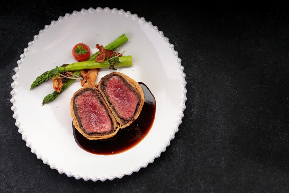 A "filet" Beef Wellington, cut open on a white plate with sauce and two pieces of asparagus.